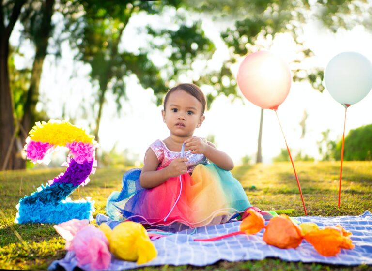 a cute baby girl in colorful dress sitting on a picnic blanket